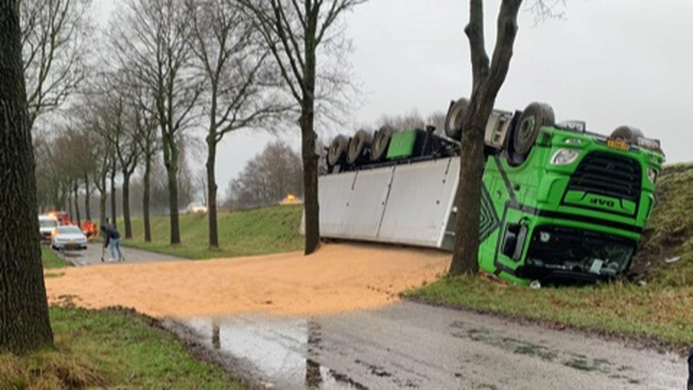 Vrachtwagen met graan belandt op de kop naast de weg